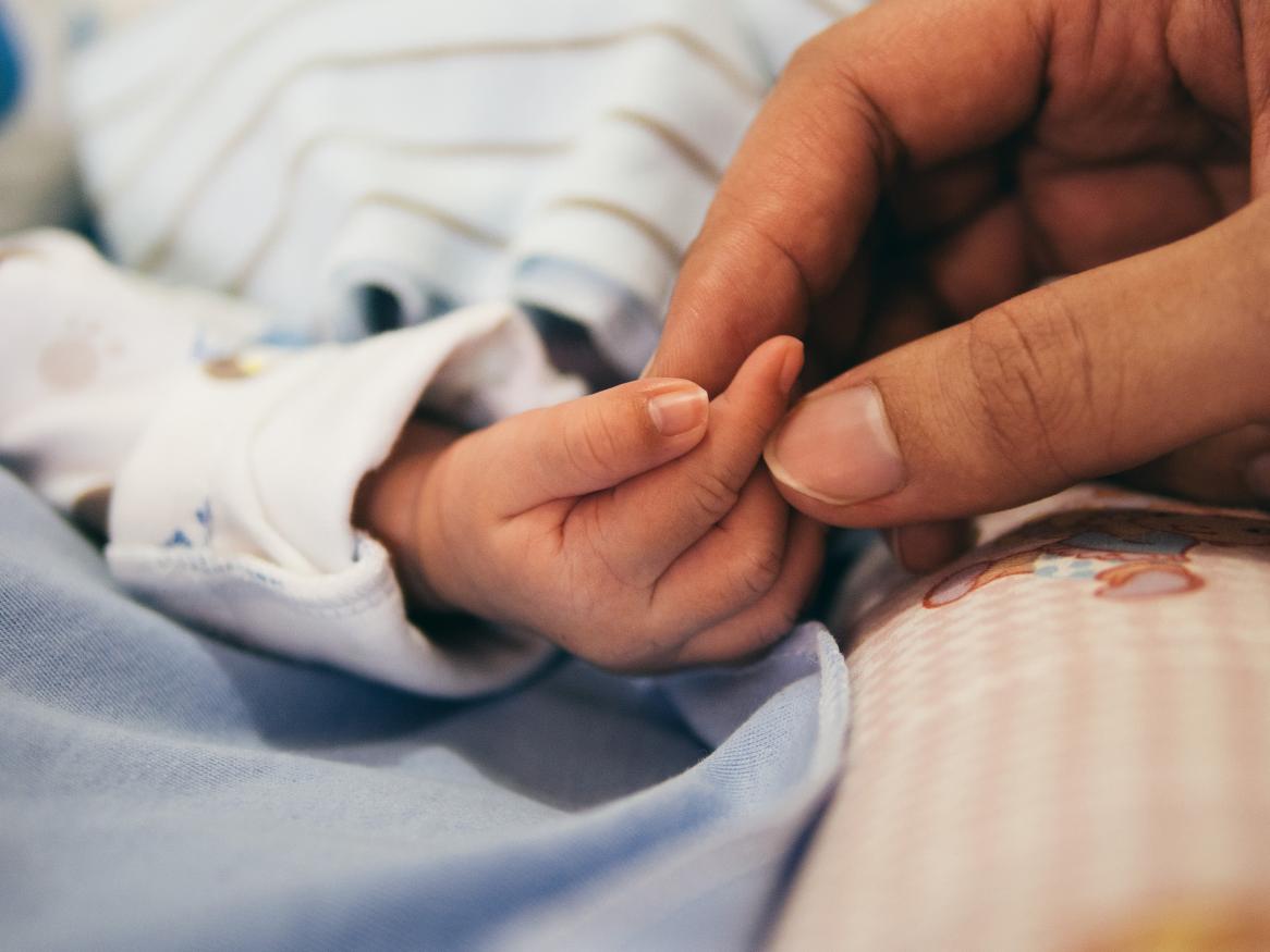 adult hand touching infant's hand