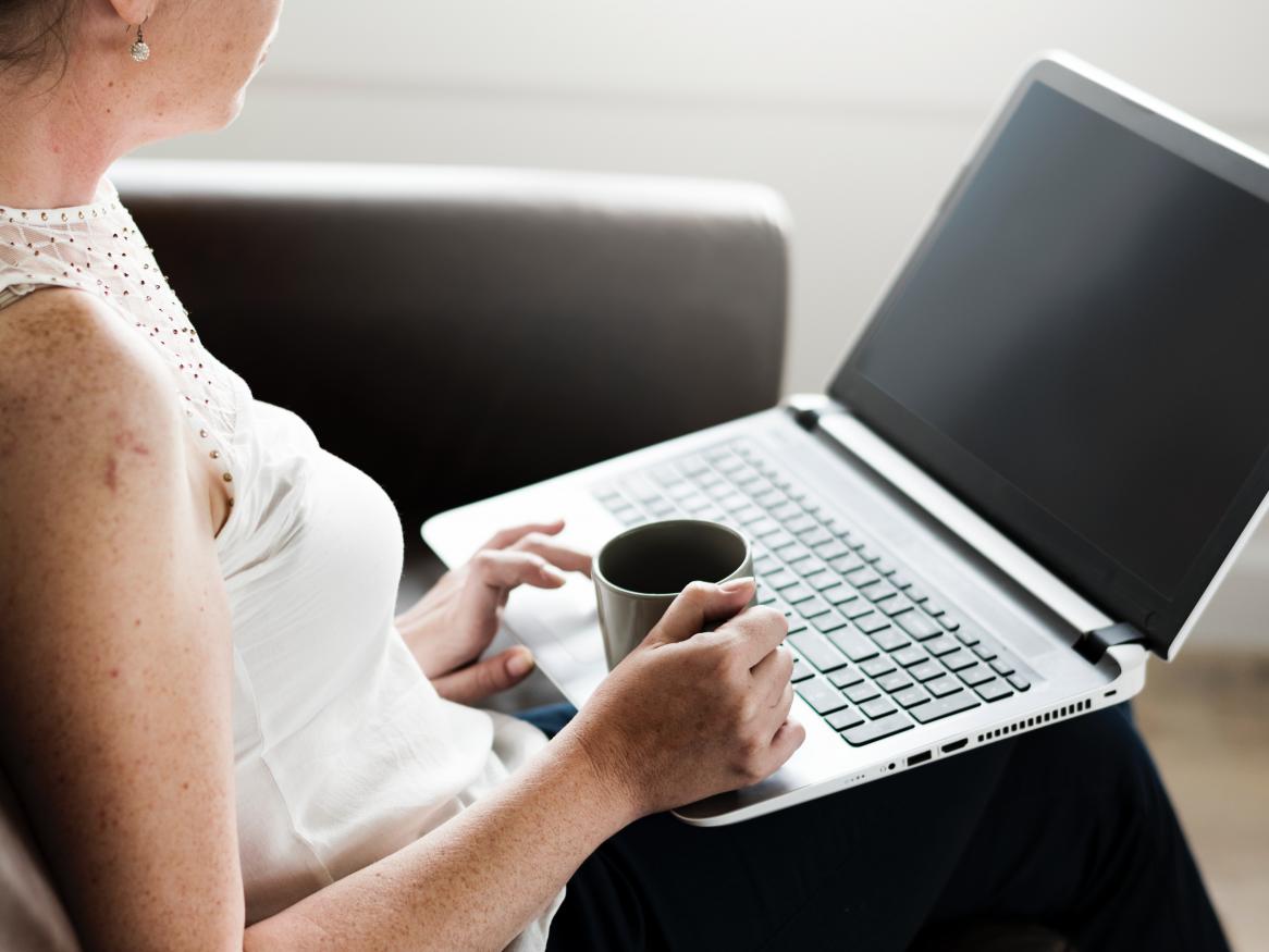 woman with coffee sitting on chair with laptop