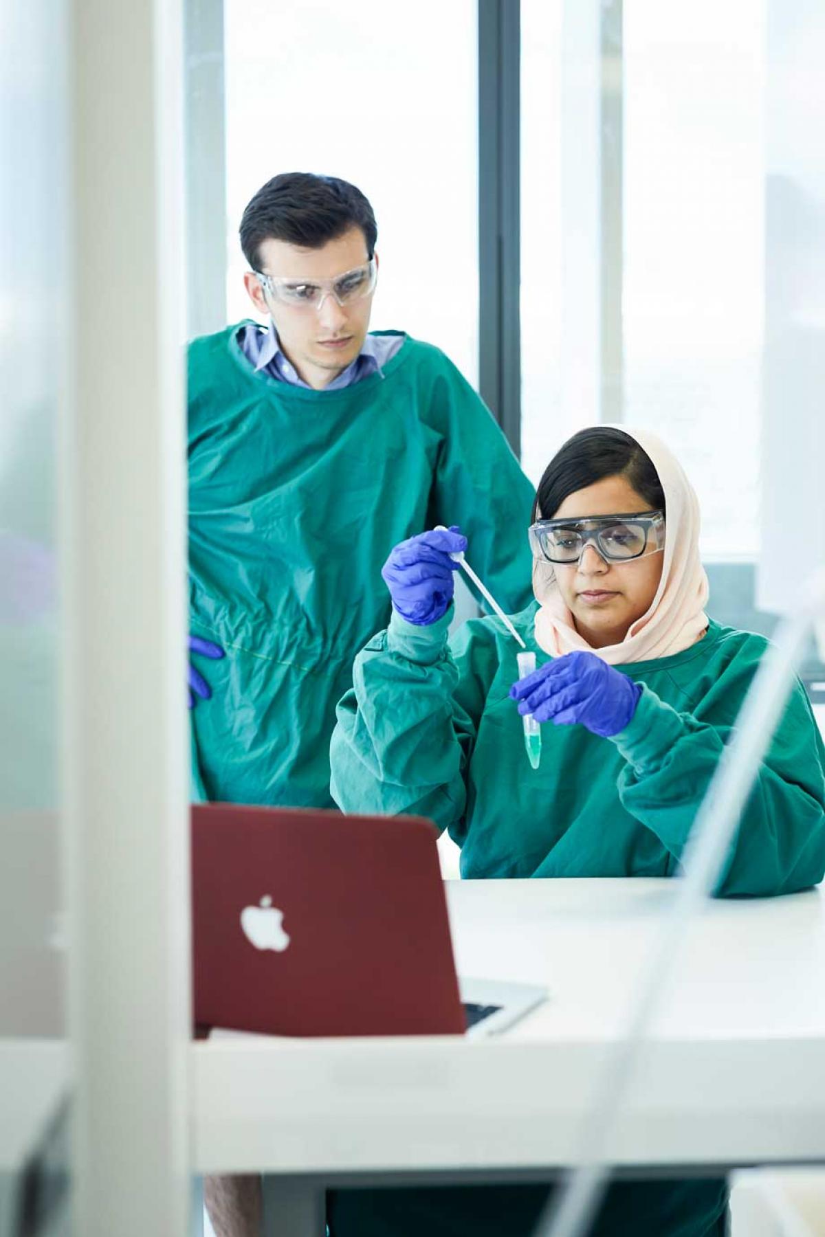 Two research students within a lab, looking at a test tube