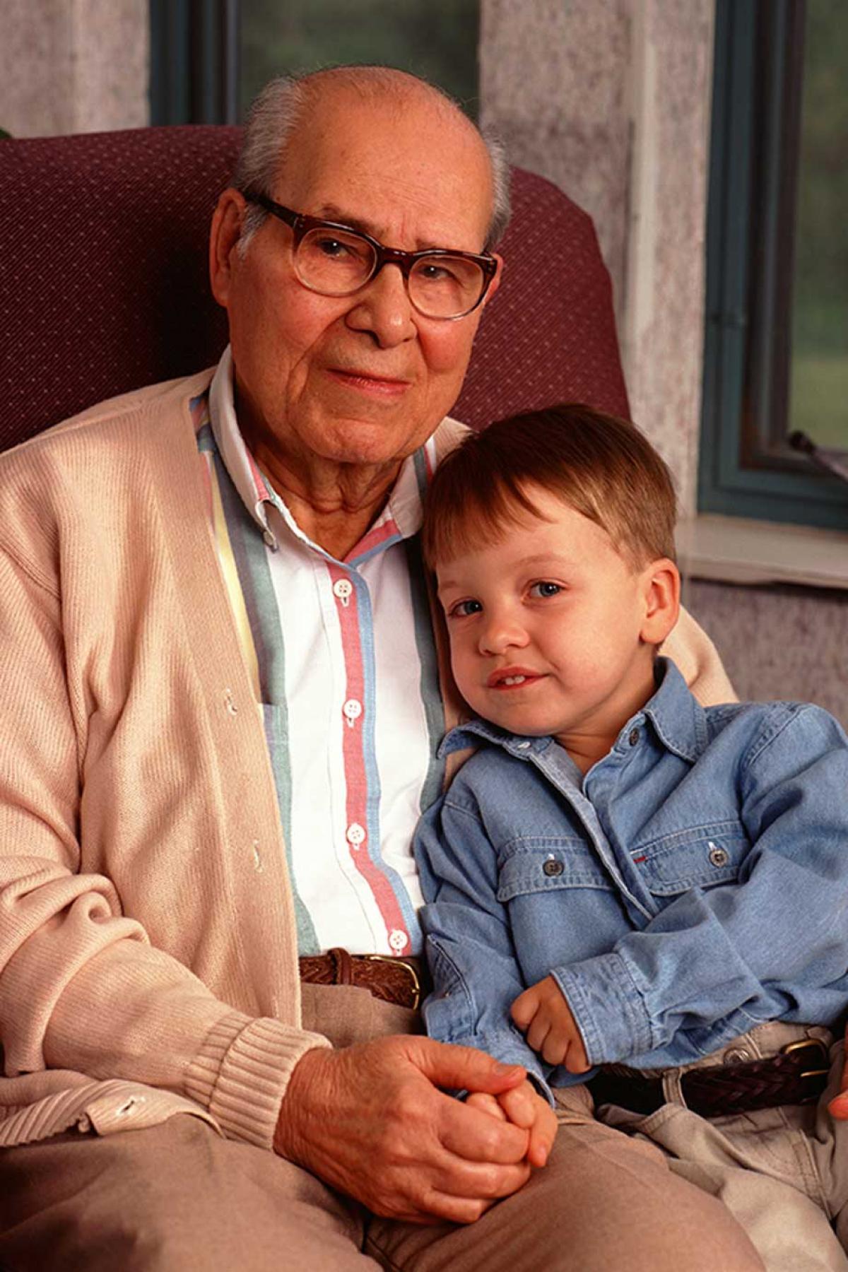 An elderly gentleman sitting in an arm chair with a young boy 