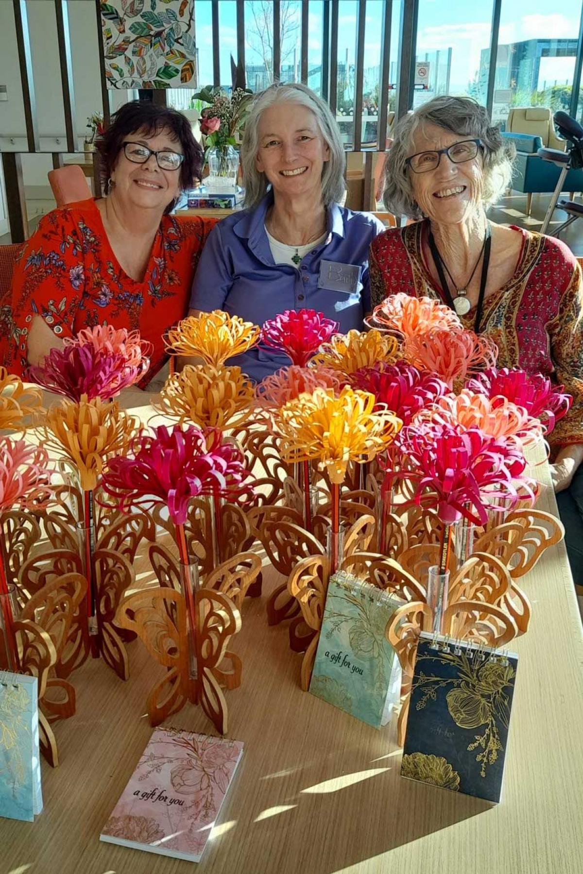 3 smiling women sitting behind a table of flowers