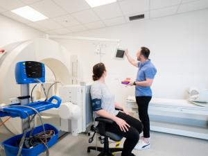 Female research study participant seated in front of gamma camera, researcher guiding her attention to the screen