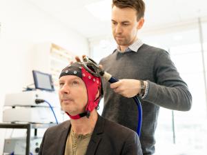 Male research study participant wearing skull cap undergoing assessment by male researcher