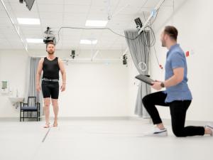 Male research study participant wearing CGI dots walking and being monitored in gait lab by researcher