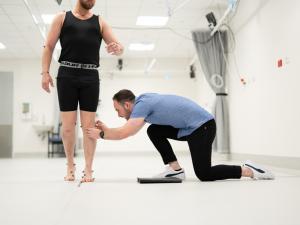 Male research study participant being fitted with CGI dots by researcher in gait lab