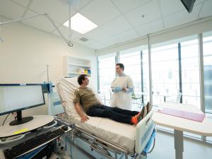 Male research study participant lying on bed in clinical room discussing procedure with researcher