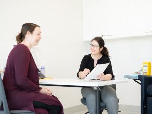 Female research study participant being interviewed by researcher at a desk in a consulting room