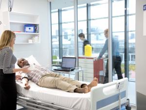 Clinical room with research study participant lying in a bed being monitored by a researcher