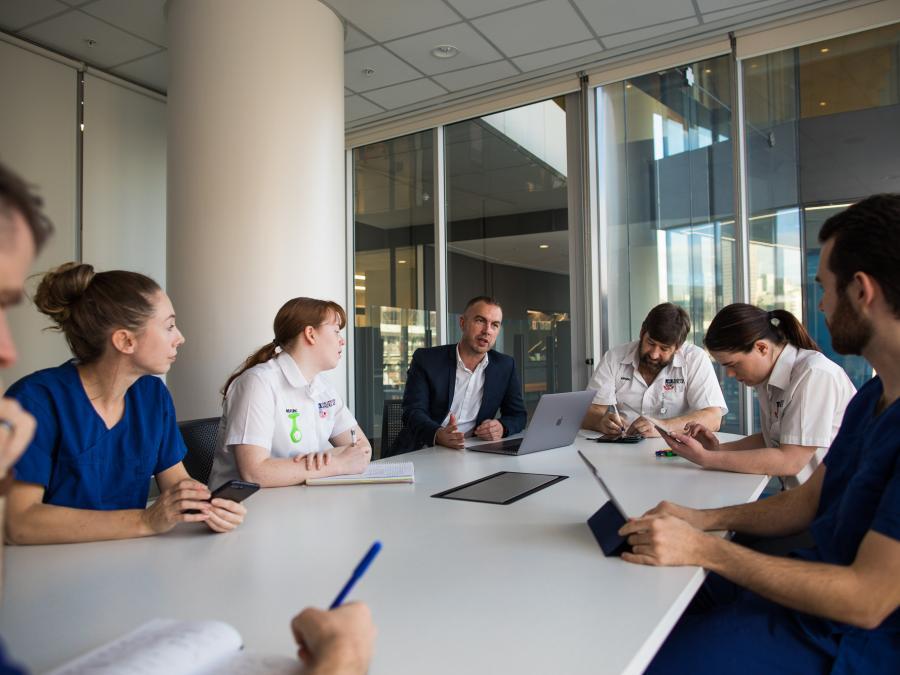 Adam Montagu talking to simulation students at a large meeting room desk