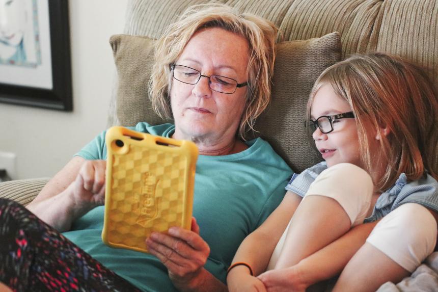 Grandmother and granddaughter sitting on couch playing hand-held game 