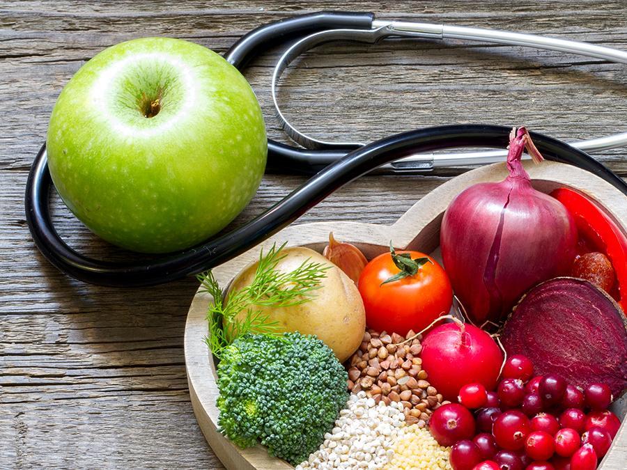 Love heart shaped bowl full of vegetables, fruit and grains, plus green apple and stethoscope