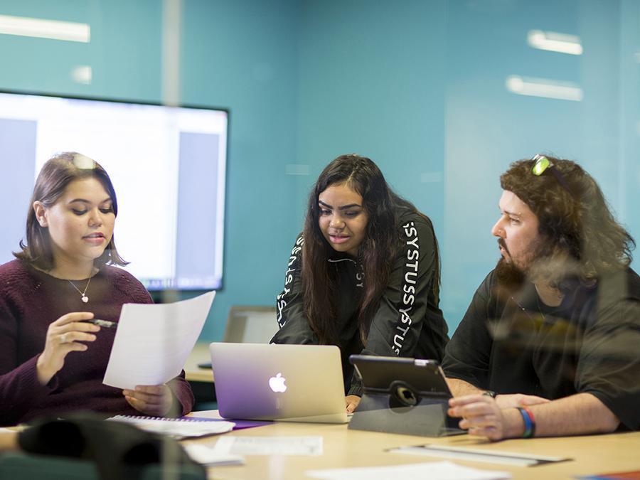 Three students sitting at a desk with a laptop