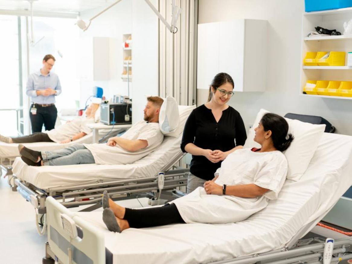 3-bay clinical bed room with research patients in beds, tended to by two researchers