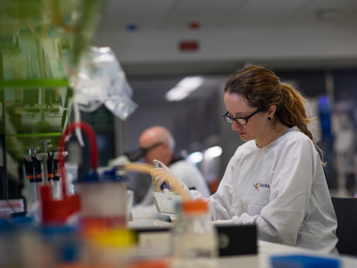Female researcher in white lab coat seated in wet lab