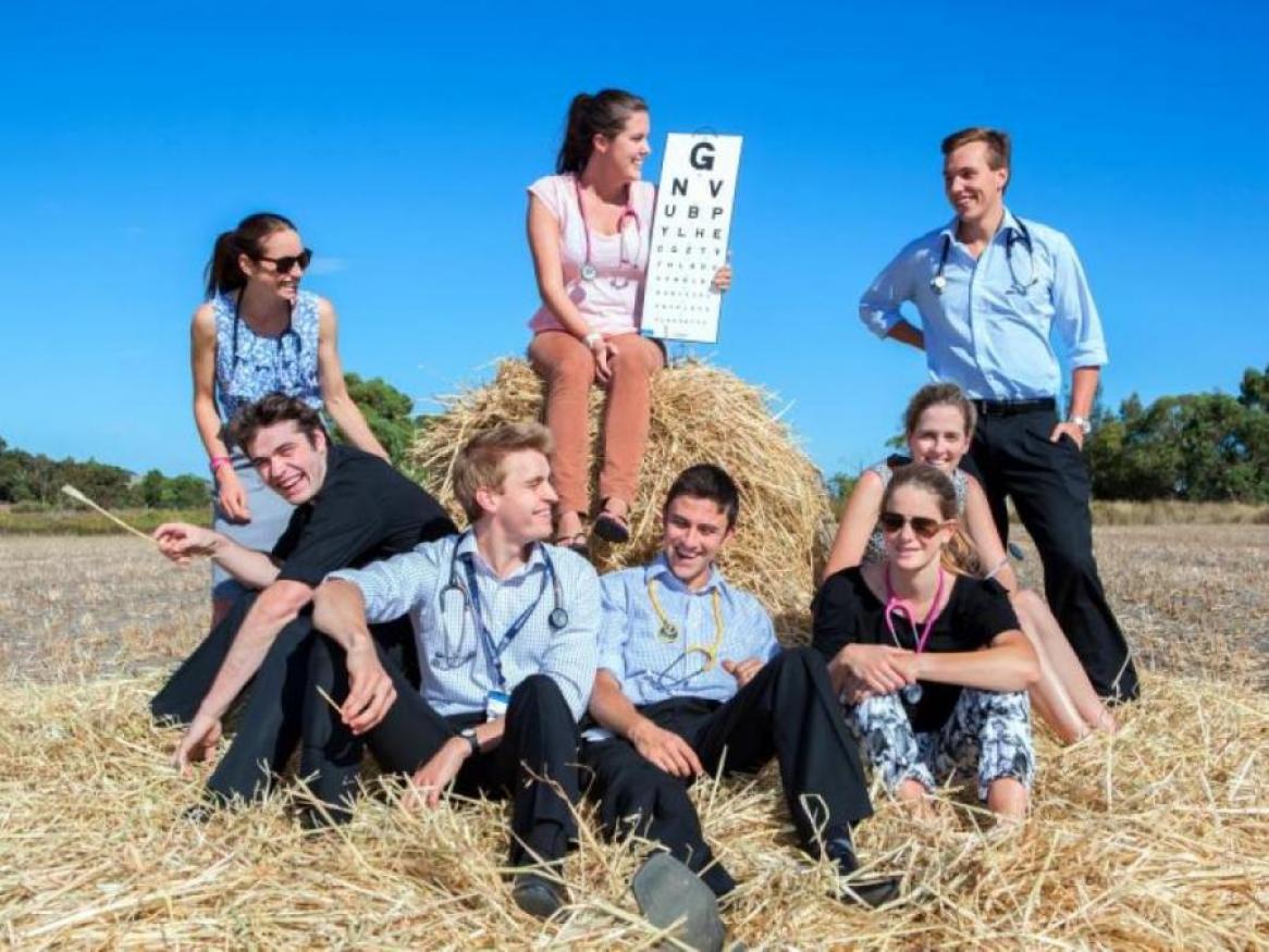 Eight students sitting on hay bale, smiling, one student holding up with eye chart