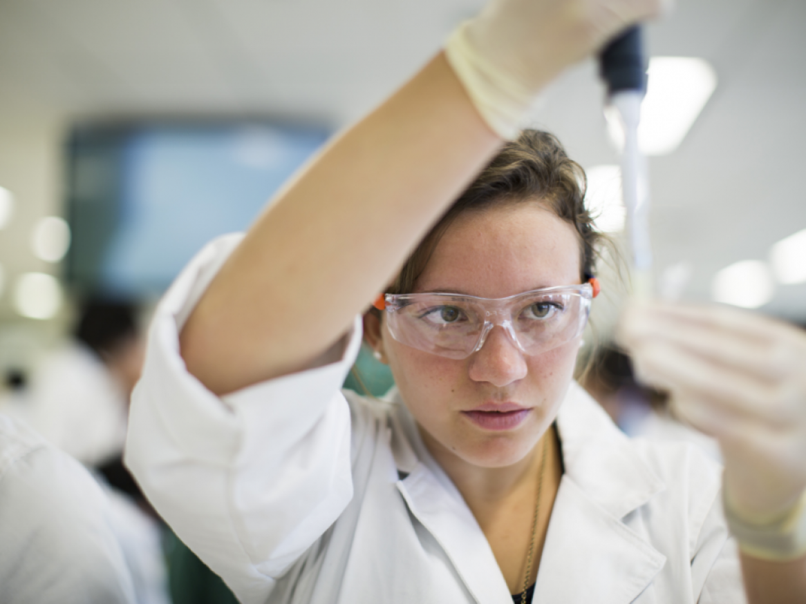 Researcher in lab coat and safety glasses using laboratory apparatus
