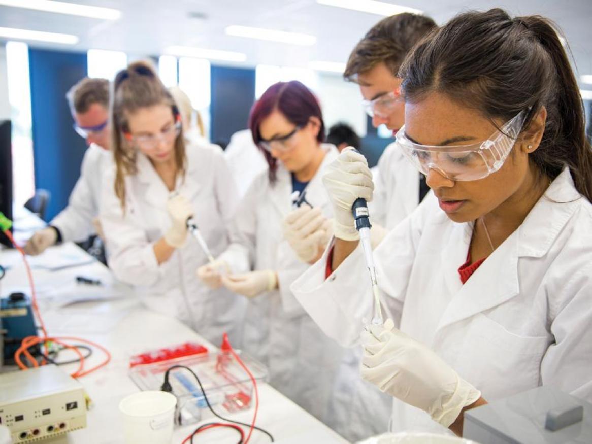 Students in white lab coats and protective glasses in lab