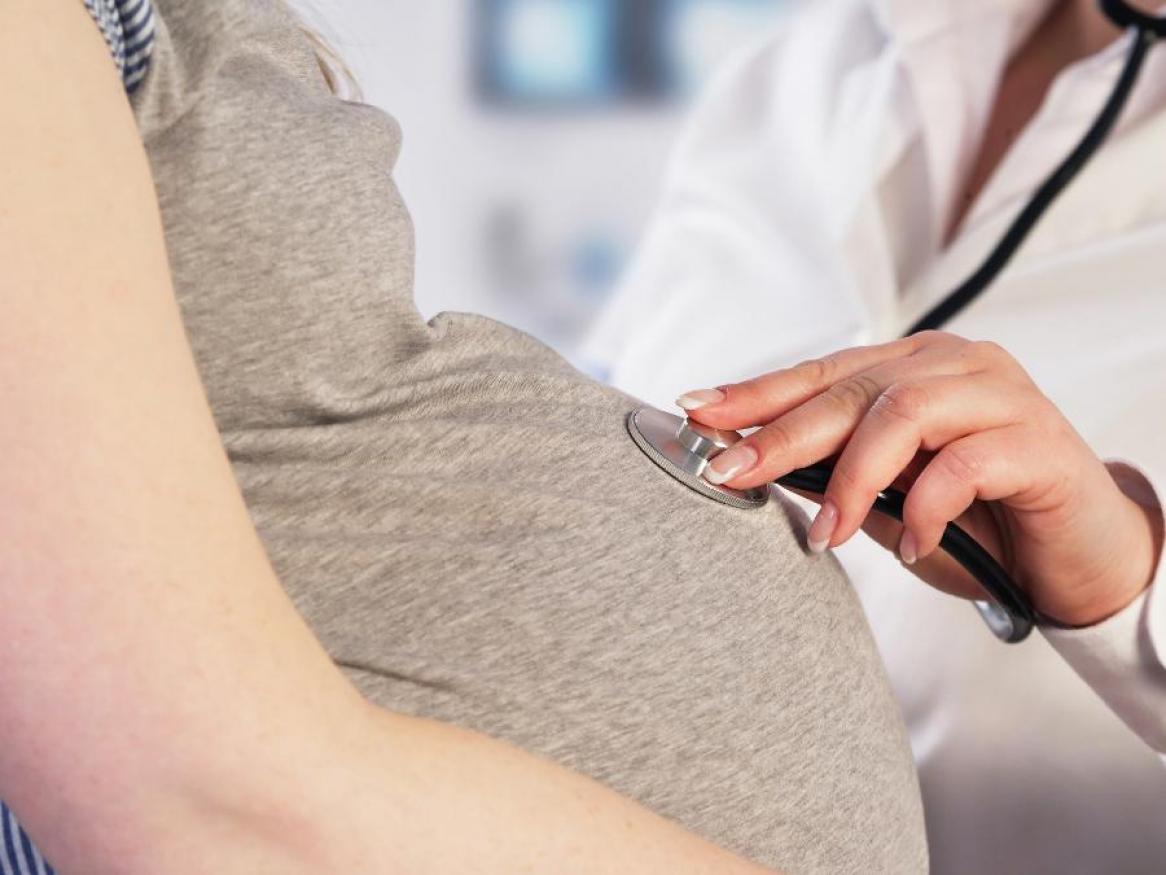 Doctor monitors pregnanct woman with stethoscope on pregnancy tummy