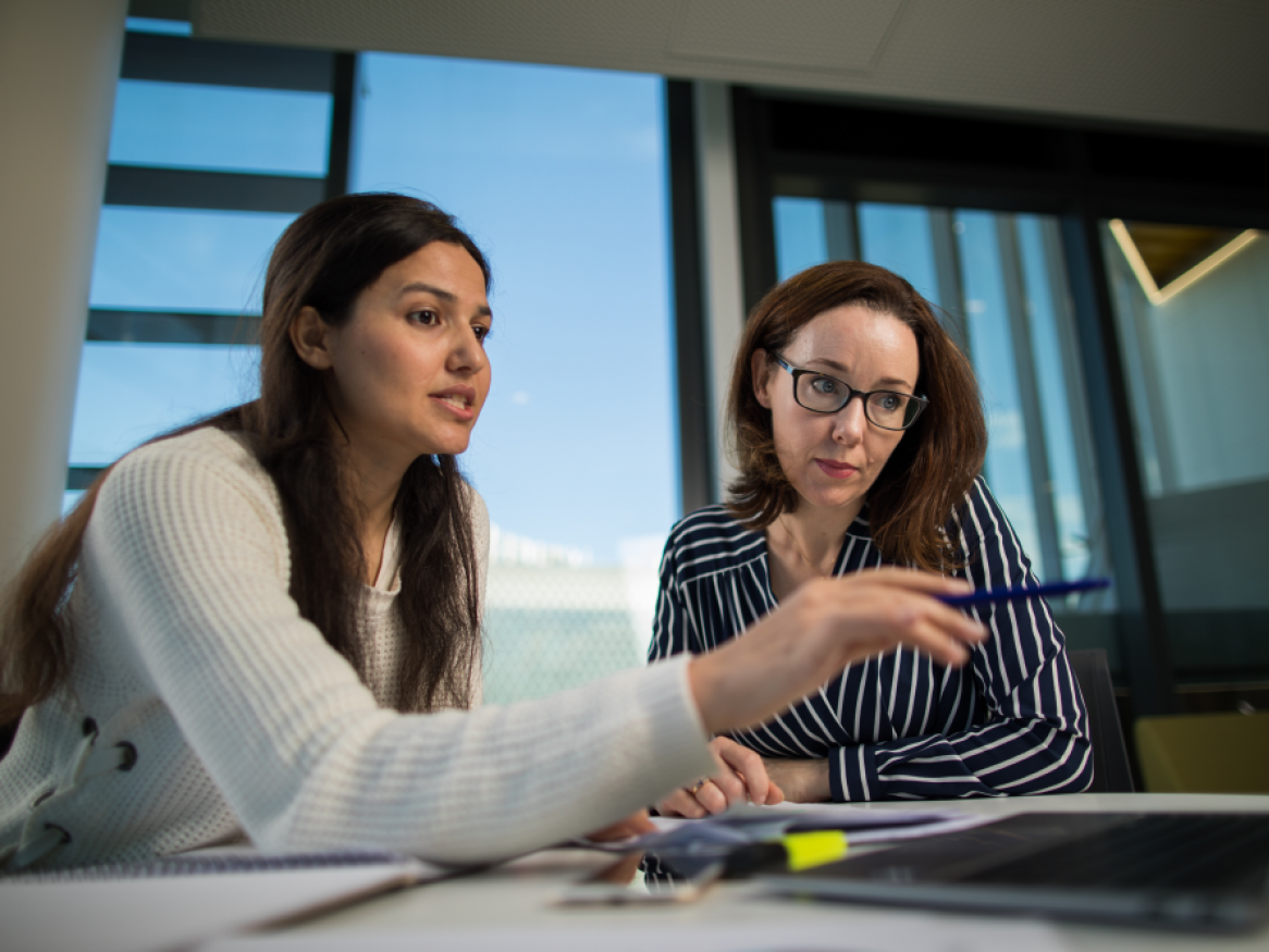 PhD student sitting with public health researcher discussing notes on a computer screen