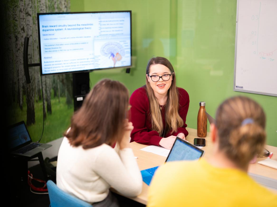Three psychology students studying together in room with green walls and large computer monitor in background